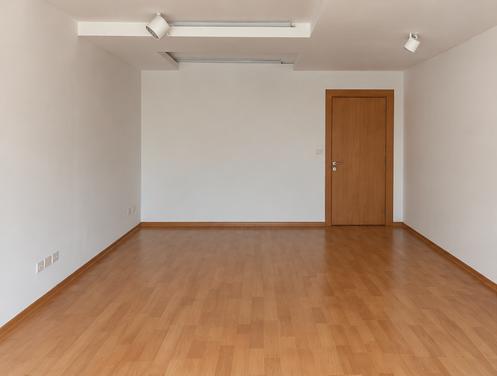 Local antes: ambiente vacío con piso de madera, paredes blancas y una puerta al fondo
